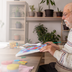 Elderly man with dementia painting at a table in a memory care setting, engaging in therapeutic, creative activity.
